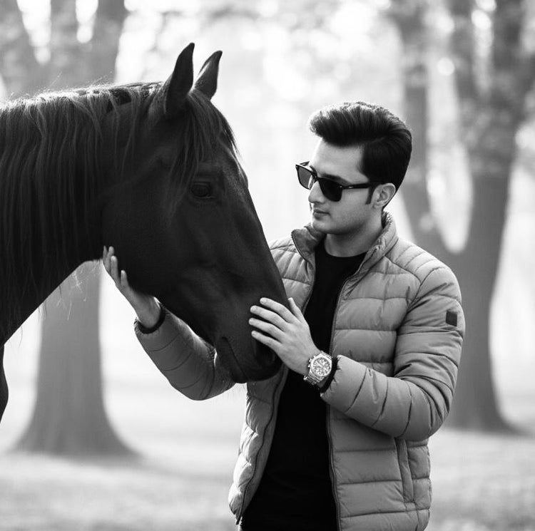 Man in a puffer jacket and sunglasses petting a horse in a forest setting